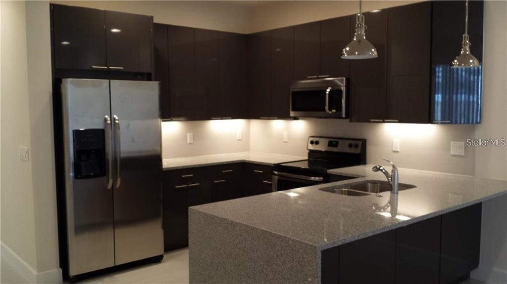 A modern kitchen features dark glossy cabinets, stainless steel appliances, and a granite-topped island — 17505 PLACIDITY AVENUE, CLERMONT, FL