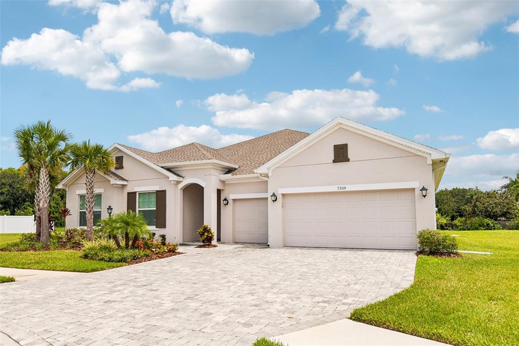 A single-story house with a beige stucco exterior, a paved driveway, and a three-car garage — 7510 ASHBROOKE PINE LOOP, ODESSA, FL