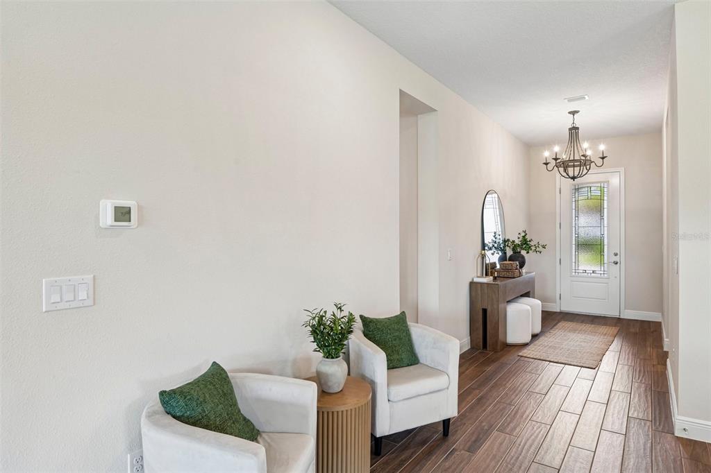 A bright entryway features wood-look tile flooring, two white armchairs, and a decorative chandelier — 7510 ASHBROOKE PINE LOOP, ODESSA, FL