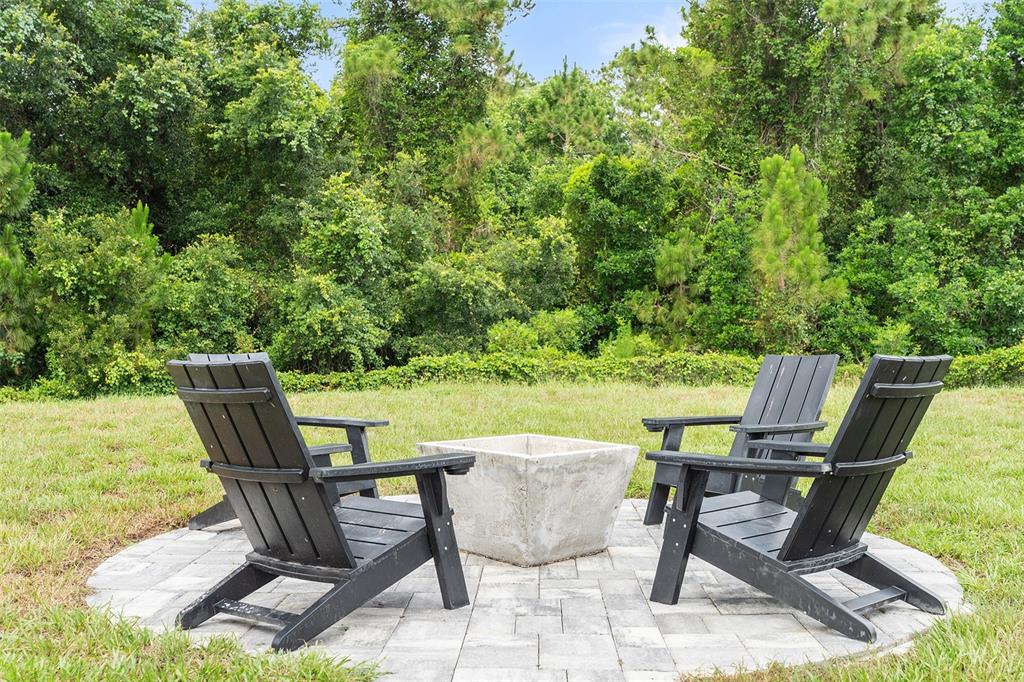 Two black Adirondack chairs sit on a stone patio around a square concrete fire pit — 3481 MIDDLEBROOK PL, ST CLOUD, FL