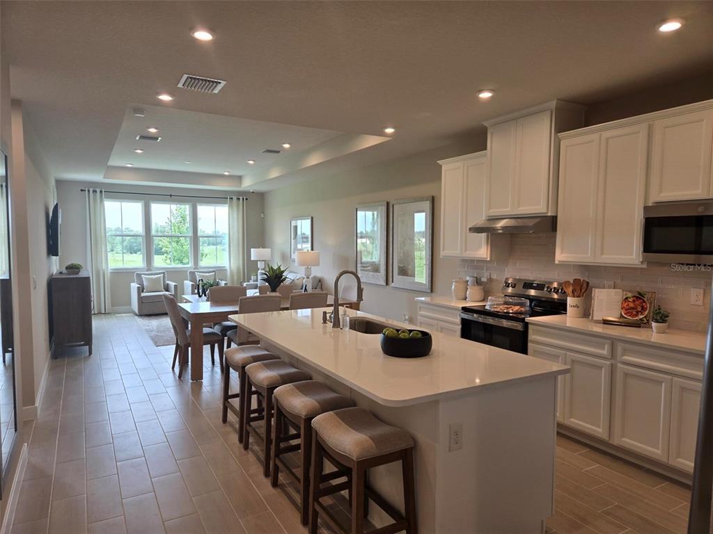 A modern kitchen with white cabinets and a large island overlooks an open dining area — 18857 EMERALD SUMMIT DRIVE, SPRING HILL, FL