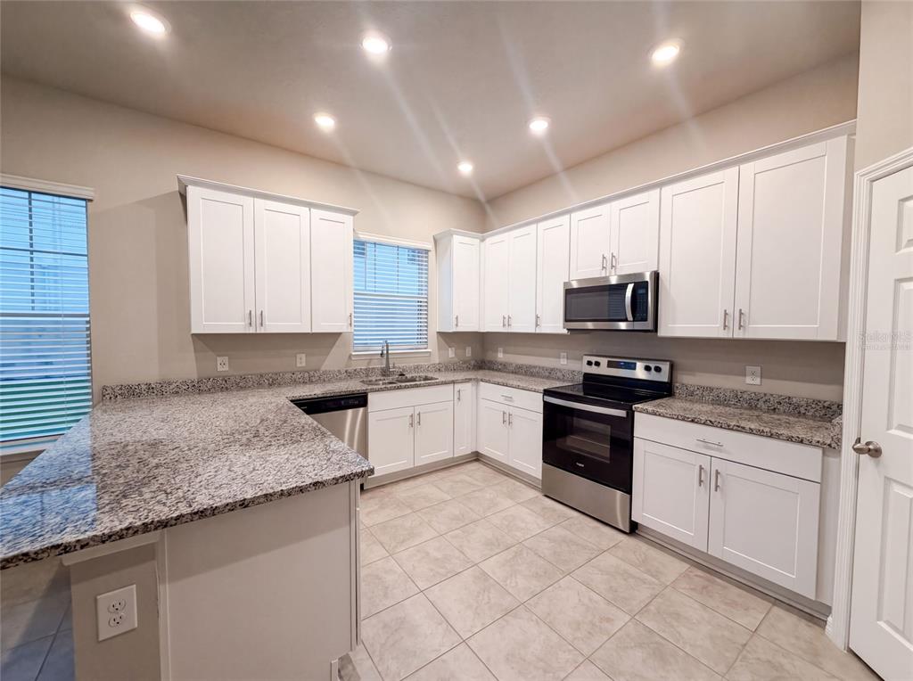 A kitchen with white cabinets, granite countertops, stainless steel appliances, and tile flooring — 538 VENETIAN PALMS BOULEVARD, NEW SMYRNA BEACH, FL