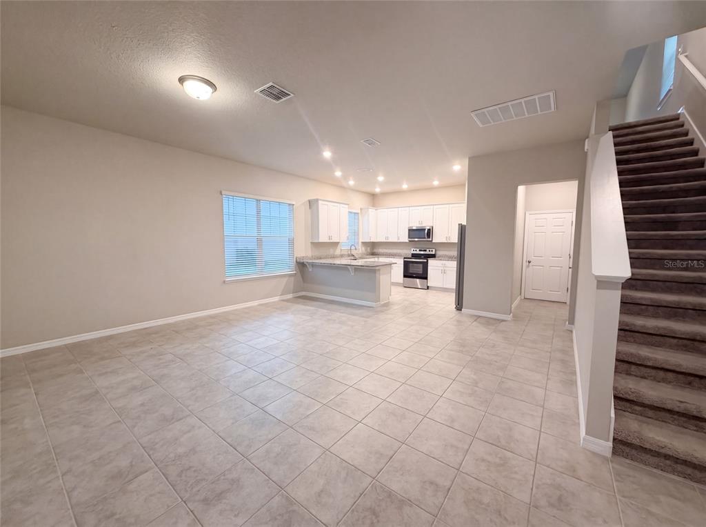 An open-concept kitchen and living area features tile flooring, white cabinetry, and a carpeted staircase — 538 VENETIAN PALMS BOULEVARD, NEW SMYRNA BEACH, FL