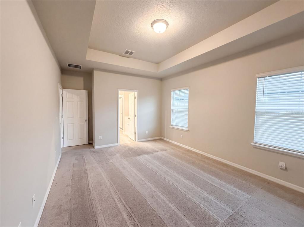 An empty bedroom features beige walls, carpeted flooring, a tray ceiling, and two doorways — 538 VENETIAN PALMS BOULEVARD, NEW SMYRNA BEACH, FL