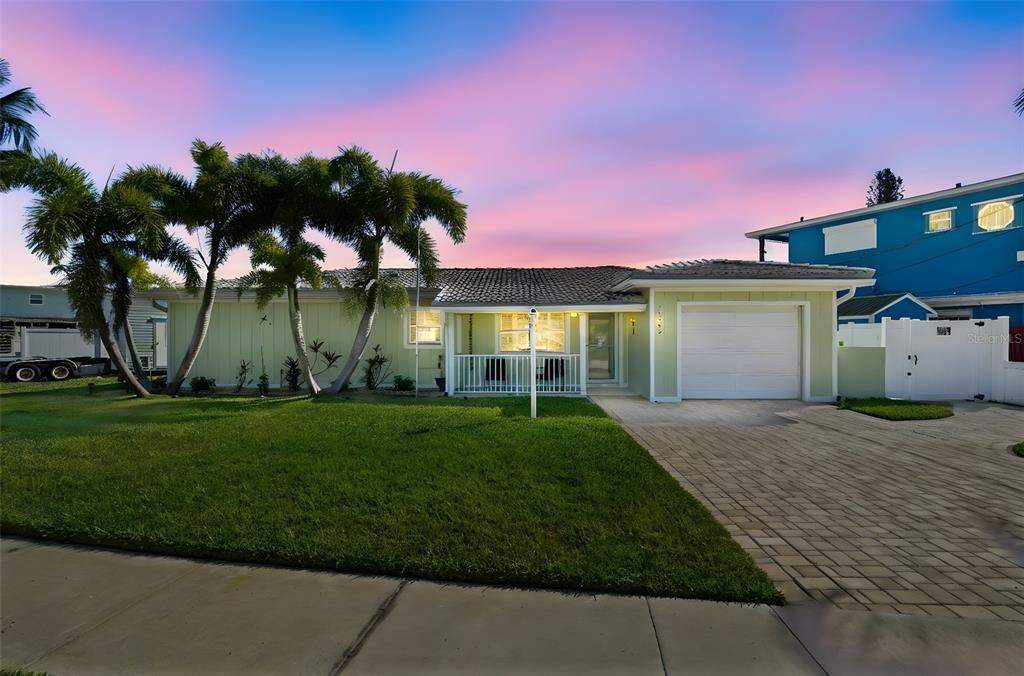 A single-story house with a paved driveway, a white garage, and palm trees at sunset — 15302 HARBOR DRIVE, MADEIRA BEACH, FL