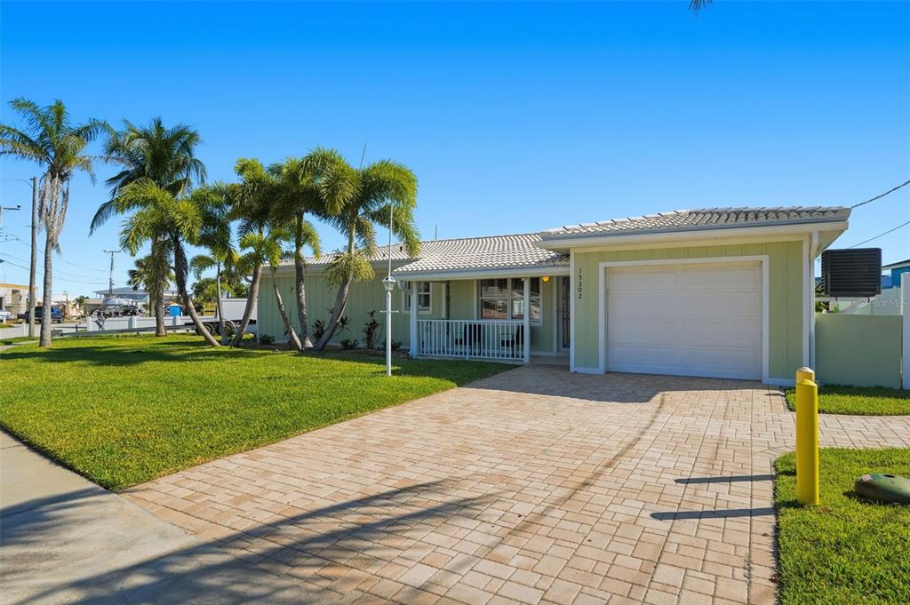 A light green single-story house features a white garage door and a paved driveway — 15302 HARBOR DRIVE, MADEIRA BEACH, FL