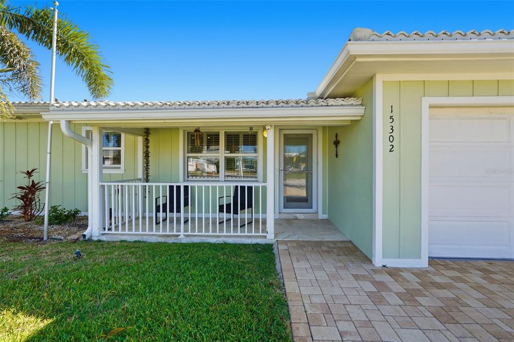 A light green house exterior features a covered front porch, white railing, and paver walkway — 15302 HARBOR DRIVE, MADEIRA BEACH, FL