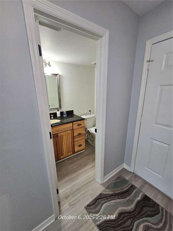 A bathroom with a wooden vanity, black countertop, and light wood-look flooring viewed through a doorway — 6500 SUNSET WAY UNIT 308, ST PETE BEACH, FL
