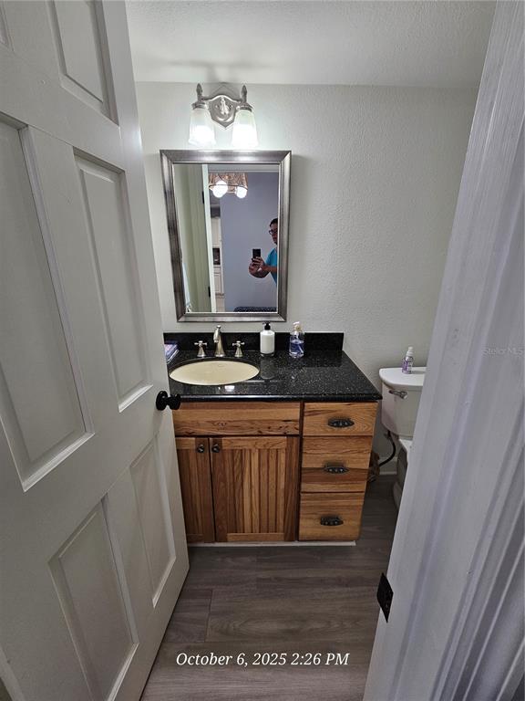 A bathroom features a wood vanity with a black countertop, a mirror, and gray flooring — 6500 SUNSET WAY UNIT 308, ST PETE BEACH, FL