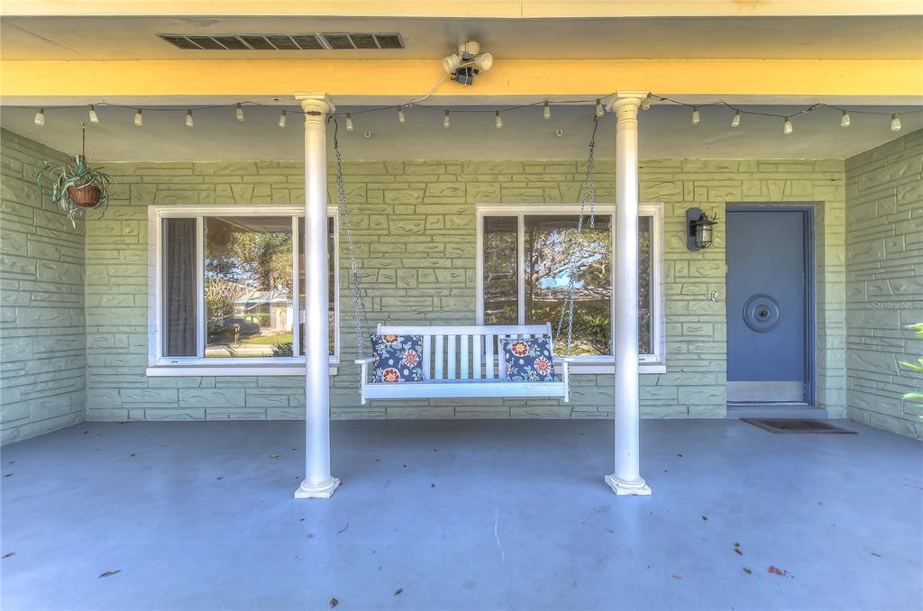 A covered front porch features a white hanging bench, light green stone walls, and columns — 5850 24TH AVENUE S, GULFPORT, FL