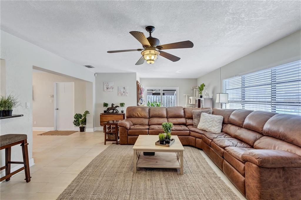 A living room features a large brown leather sectional, a coffee table, and a ceiling fan — 8532 KUMQUAT AVENUE, SEMINOLE, FL