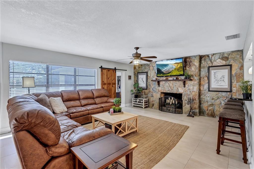 A living room features a large brown sectional sofa, a stone fireplace, and tile flooring — 8532 KUMQUAT AVENUE, SEMINOLE, FL