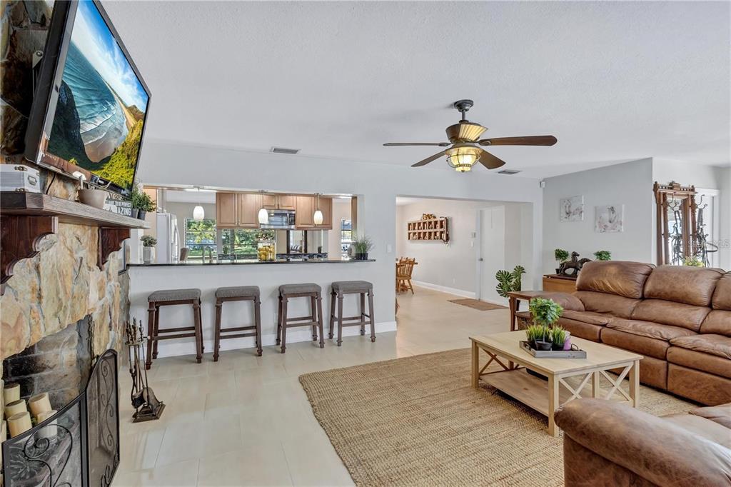 A living room with a stone fireplace, brown leather sofa, and a kitchen breakfast bar — 8532 KUMQUAT AVENUE, SEMINOLE, FL