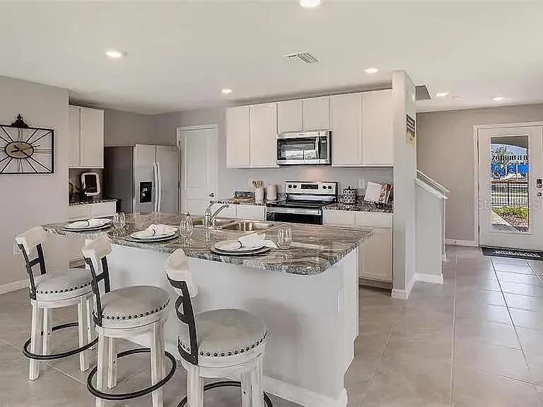 A kitchen features white cabinetry, a granite-topped island with bar stools, and tiled flooring — 11434 STONE PINE STREET, RIVERVIEW, FL