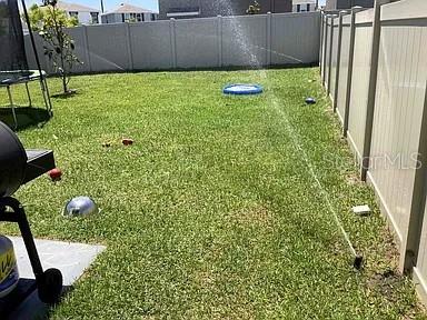 A backyard features a green lawn, a sprinkler, a trampoline, and a white privacy fence — 11434 STONE PINE STREET, RIVERVIEW, FL