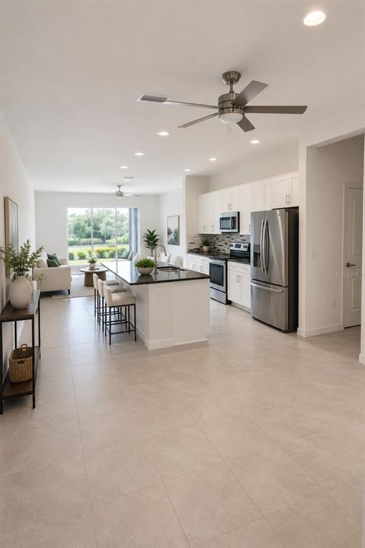 An open-concept kitchen and living area features white cabinetry, stainless steel appliances, and tile flooring — 8695 CANYON CREEK TRAIL, PARRISH, FL
