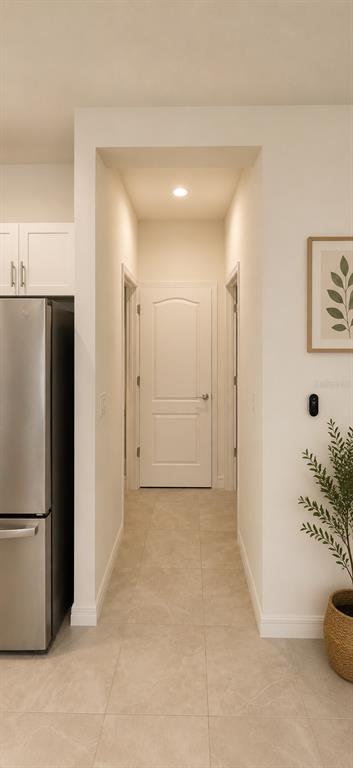 A hallway with light tile flooring leads to a white door between a kitchen and wall — 8695 CANYON CREEK TRAIL, PARRISH, FL