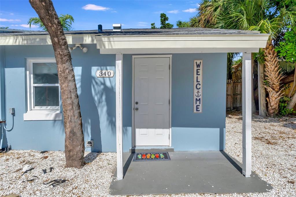 The exterior of a light blue house features a white door, a welcome sign, and gravel — 340 78TH AVENUE, ST PETE BEACH, FL