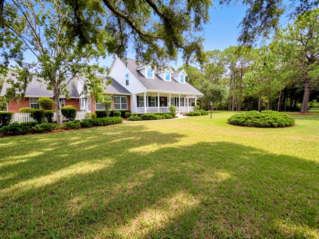 A paved driveway leads through an open gate toward a house framed by large trees — 20011 65TH AVENUE E, BRADENTON, FL