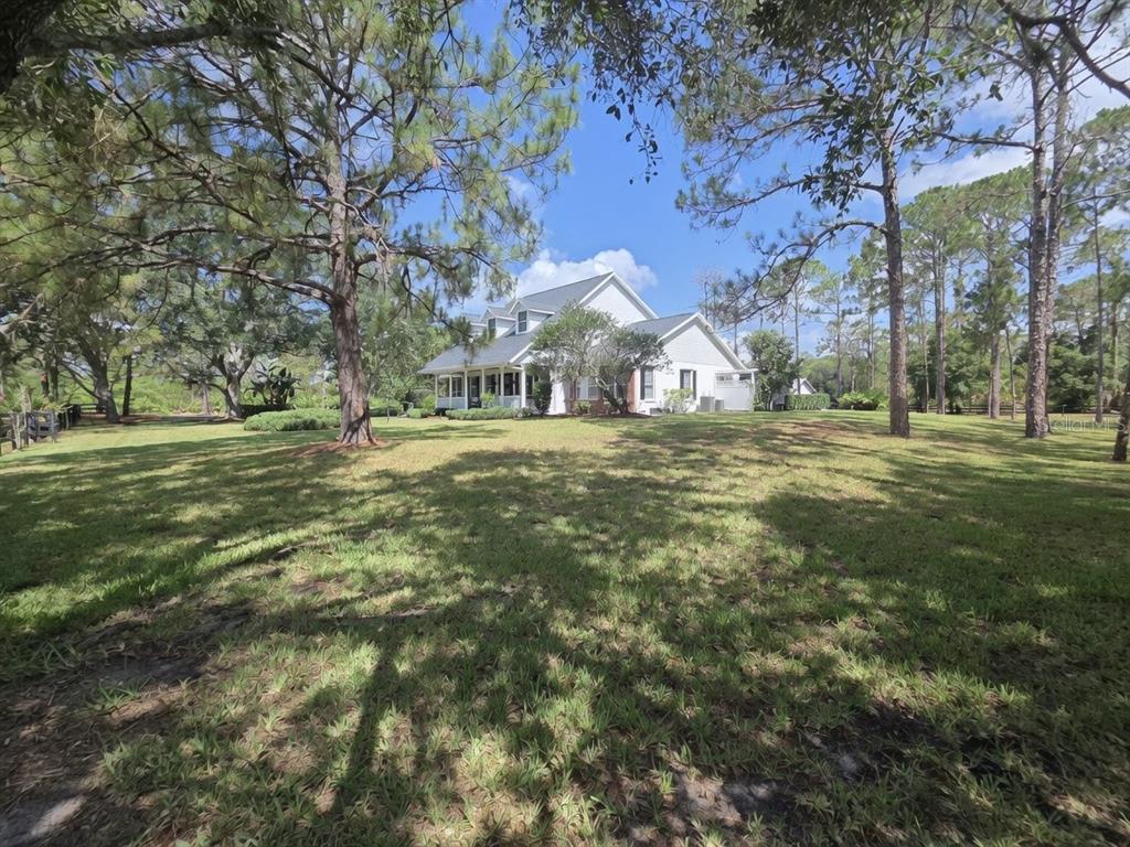 A white two-story house sits on a large, grassy lot surrounded by tall pine trees — 20011 65TH AVENUE E, BRADENTON, FL