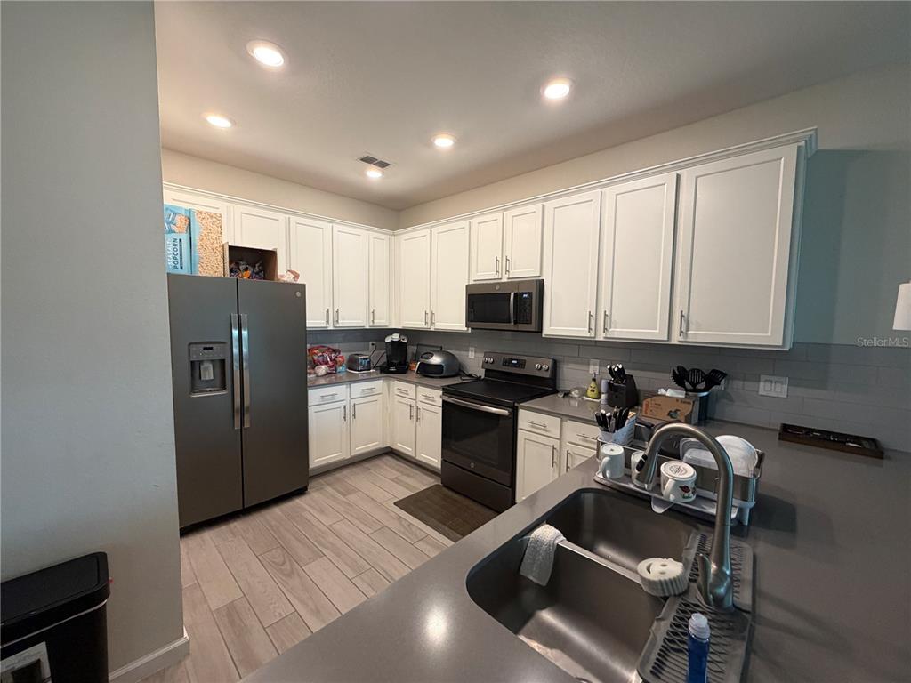 A kitchen features white cabinetry, stainless steel appliances, gray countertops, and wood-look tile flooring — 9896 RED EAGLE DRIVE, ORLANDO, FL