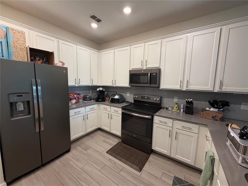 A kitchen features white cabinets, gray countertops, stainless steel appliances, and light wood-look tile flooring — 9896 RED EAGLE DRIVE, ORLANDO, FL