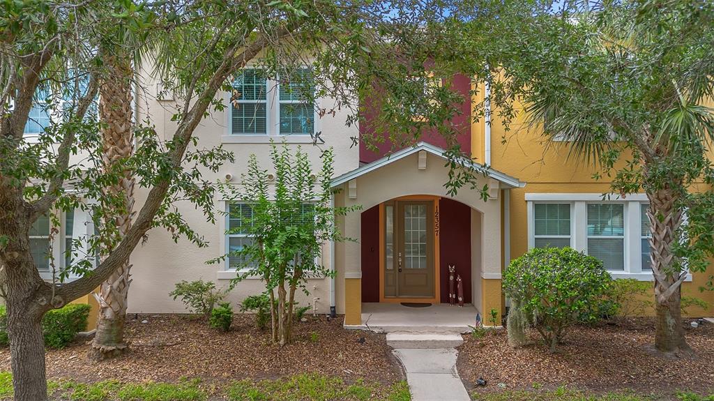 A two-story townhouse exterior features a tan and yellow facade with a red entryway — 12357 VIA DERNA PLACE, WINDERMERE, FL