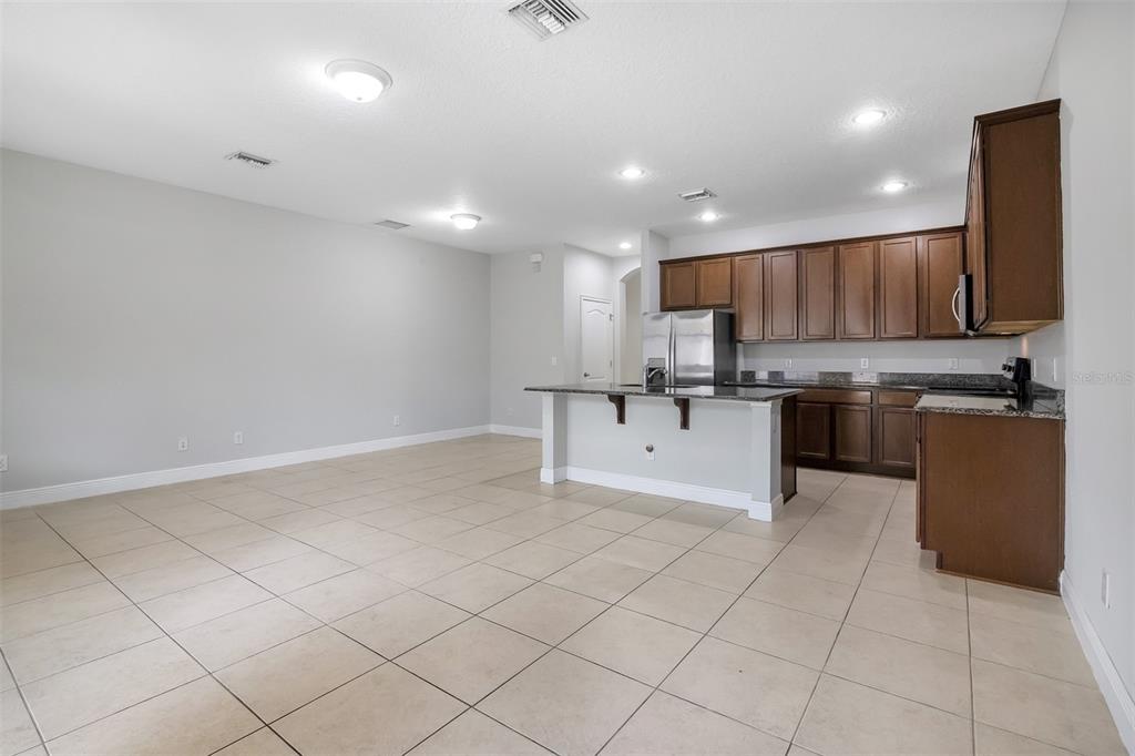 An open-concept kitchen and living area features tile flooring, dark wood cabinetry, and granite countertops — 12357 VIA DERNA PLACE, WINDERMERE, FL