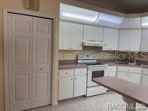 A kitchen features white cabinets, a white stove, and a light-colored countertop with a breakfast bar — 824 WINDERMERE BOULEVARD, INVERNESS, FL
