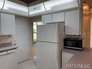 A kitchen features white cabinets, a white refrigerator, a microwave, and a door to the outside — 824 WINDERMERE BOULEVARD, INVERNESS, FL