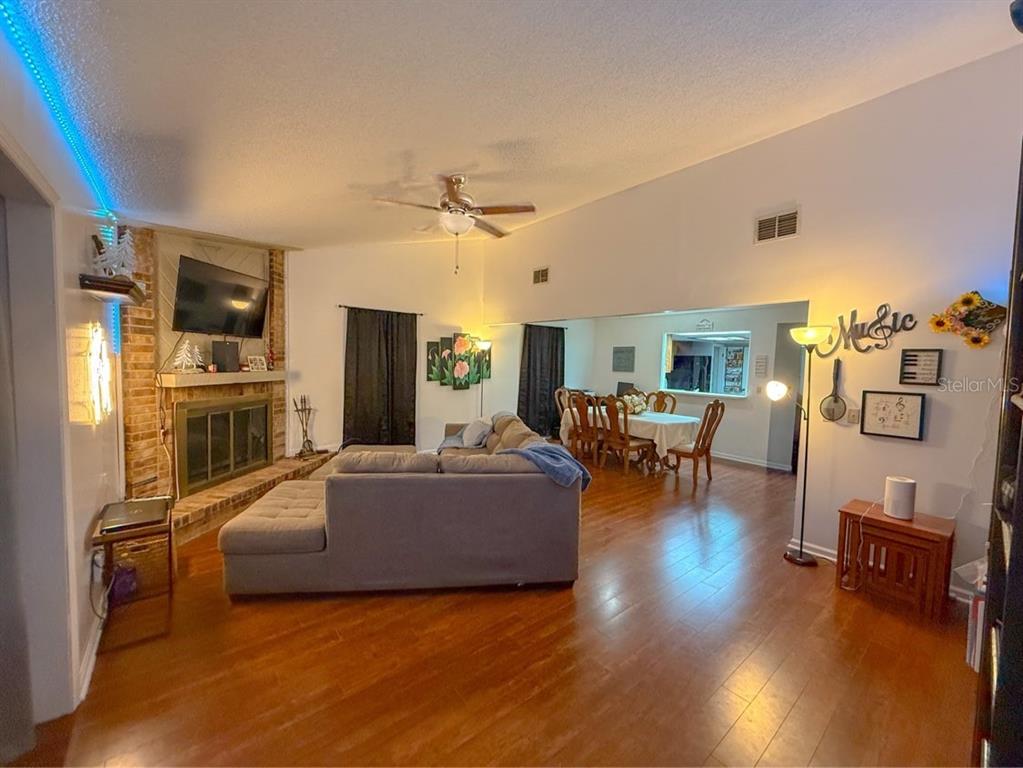 A living room with a brick fireplace, hardwood floors, and an adjacent dining area — 35058 WHISPERING OAKS BOULEVARD, DADE CITY, FL
