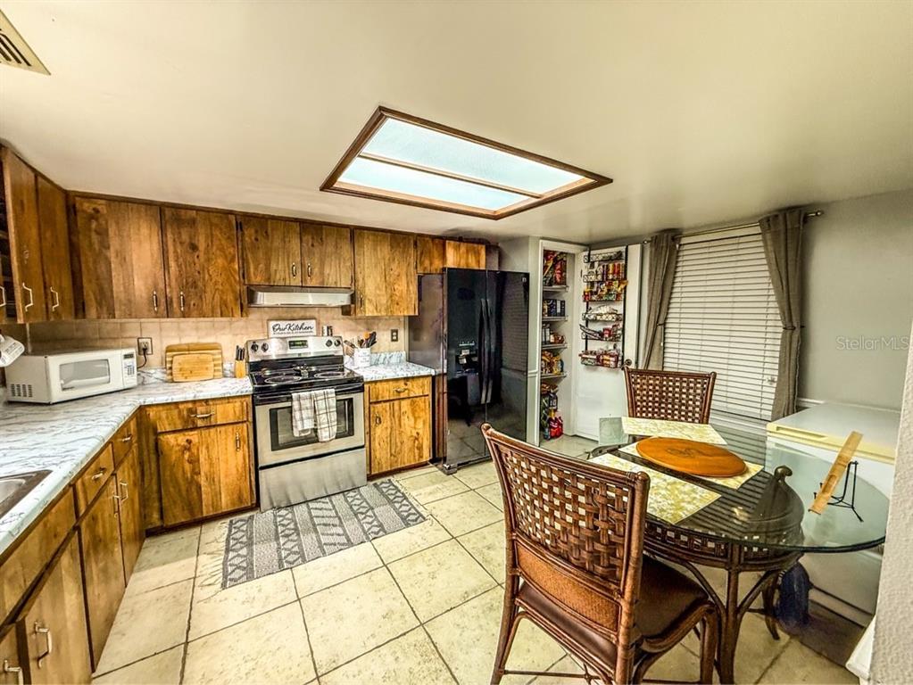 A kitchen features wood cabinets, stainless steel appliances, tile flooring, and a dining area — 35058 WHISPERING OAKS BOULEVARD, DADE CITY, FL