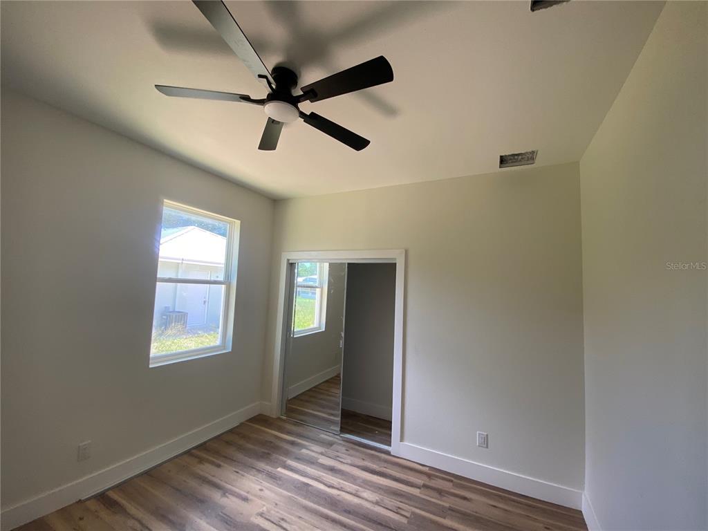 A bedroom with wood-look flooring, a ceiling fan, and a mirrored sliding closet door — 410 CITROEN DRIVE, SEBRING, FL