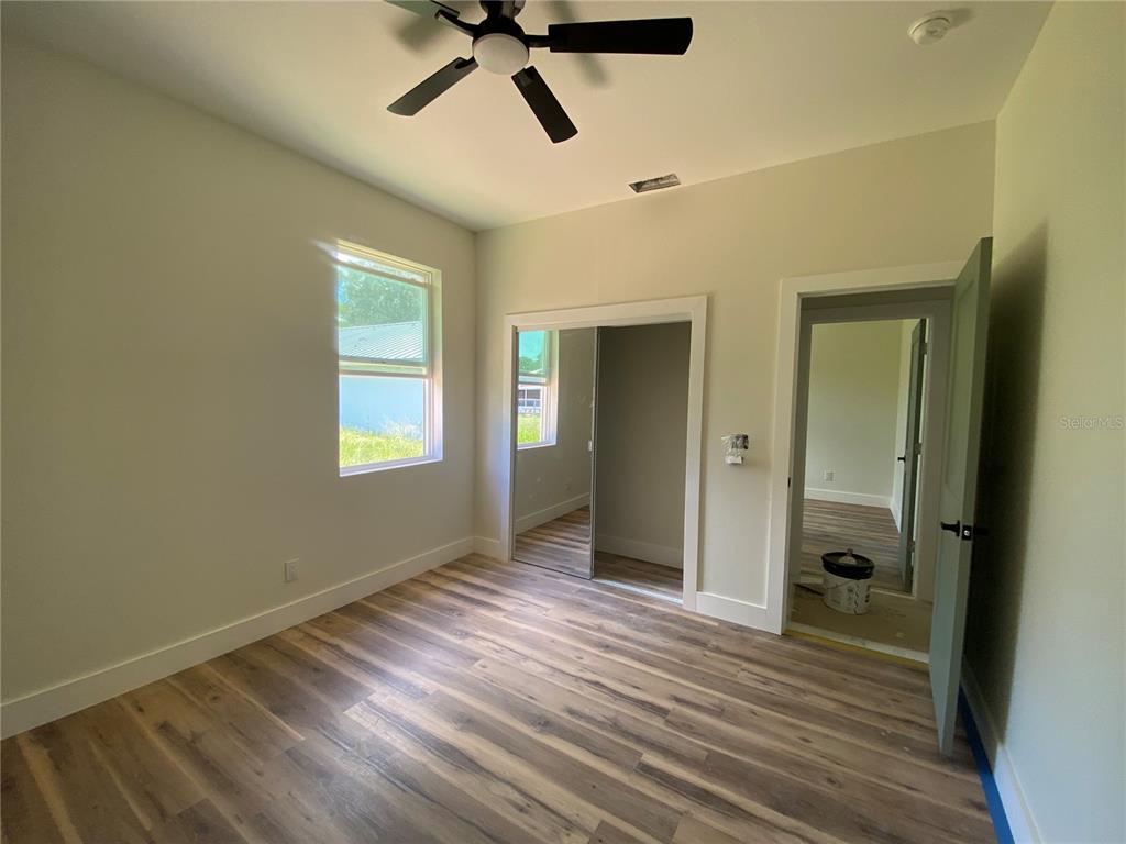 A bedroom features wood-look flooring, a ceiling fan, a mirrored closet, and an open doorway — 410 CITROEN DRIVE, SEBRING, FL