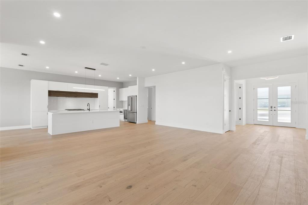 A modern open-concept kitchen and living area with white cabinetry, a large island, and light-colored wood floors — 1810 4TH STREET E, PALMETTO, FL