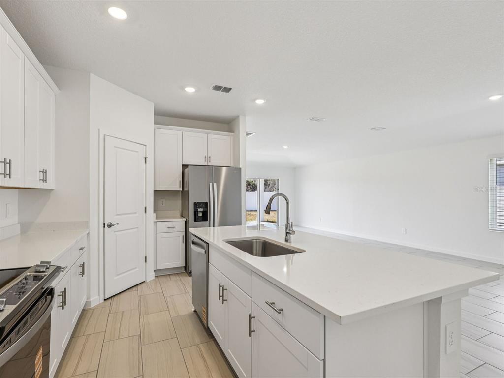 An open-concept kitchen and living area with white cabinets, stainless appliances, and tile flooring — 20 GARNI DRIVE, PALM COAST, FL
