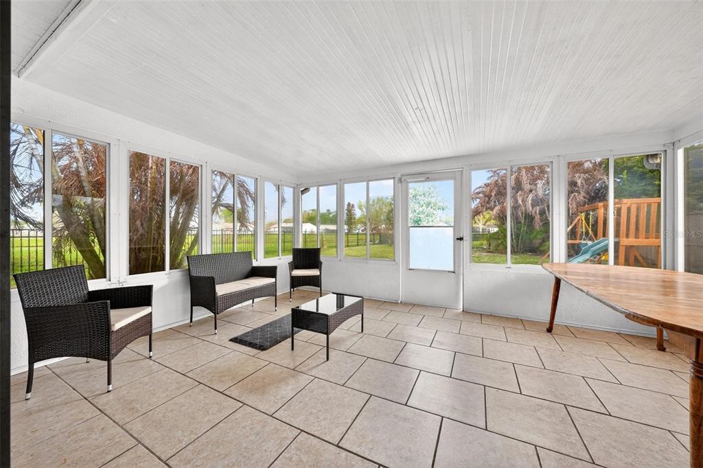 A sunroom with tiled floors, wicker furniture, and large windows overlooking a fenced backyard — 5107 DEER CREEK DRIVE, ORLANDO, FL