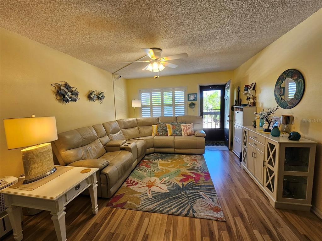 A living room features light wood flooring, yellow walls, a ceiling fan, and leather furniture — 315 30TH AVENUE W UNIT B307, BRADENTON, FL