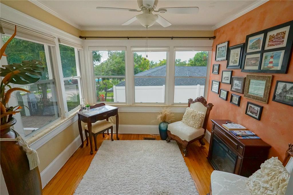 A sunroom features hardwood floors, a white rug, an orange accent wall, and large windows — 229 E 6TH AVENUE, MOUNT DORA, FL