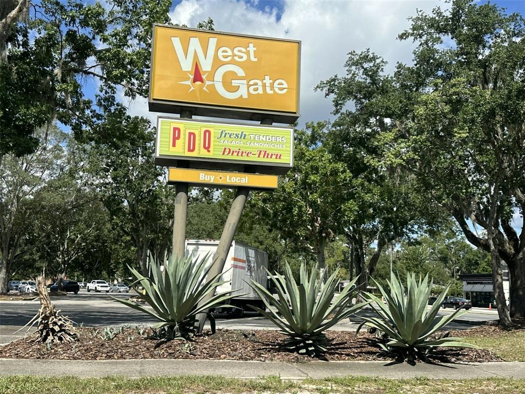 A sign for West Gate and PDQ stands behind three large agave plants outdoors — 3411 W UNIVERSITY AVENUE, GAINESVILLE, FL