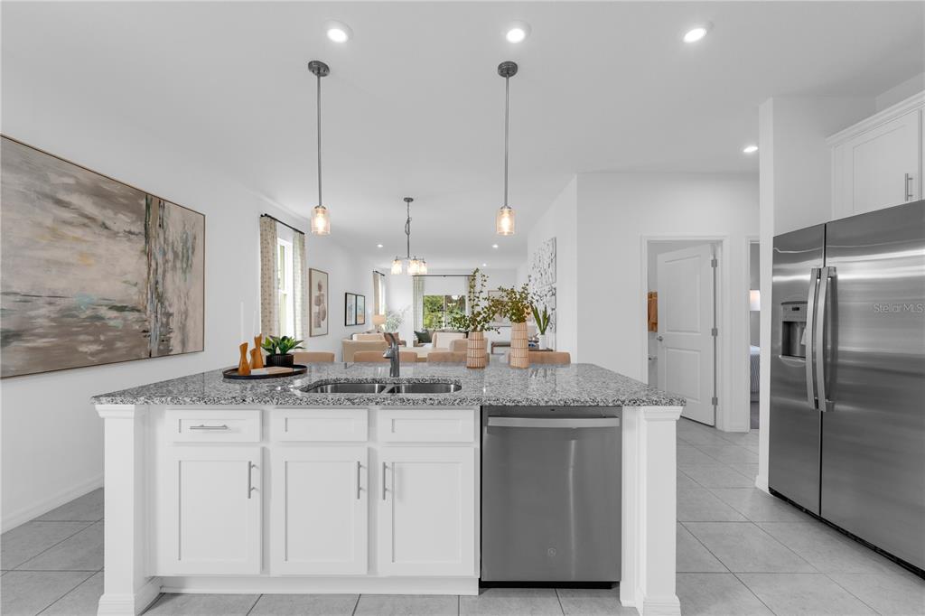 A kitchen island with granite countertops and white cabinets faces a living area — 10165 MORNING MEADOWLARK TRAIL, PARRISH, FL