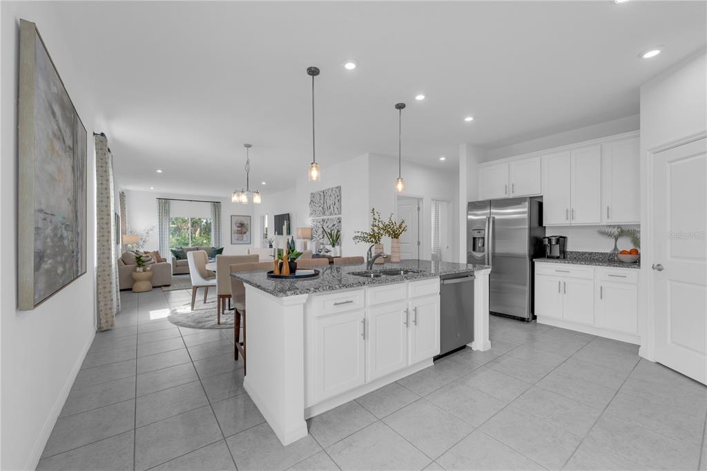 A modern kitchen with white cabinets, granite countertops, and an island opens to a living area — 10165 MORNING MEADOWLARK TRAIL, PARRISH, FL