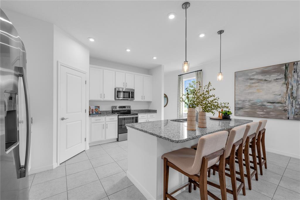 A kitchen with white cabinets, granite countertops, a center island with bar seating, and tile flooring — 10165 MORNING MEADOWLARK TRAIL, PARRISH, FL