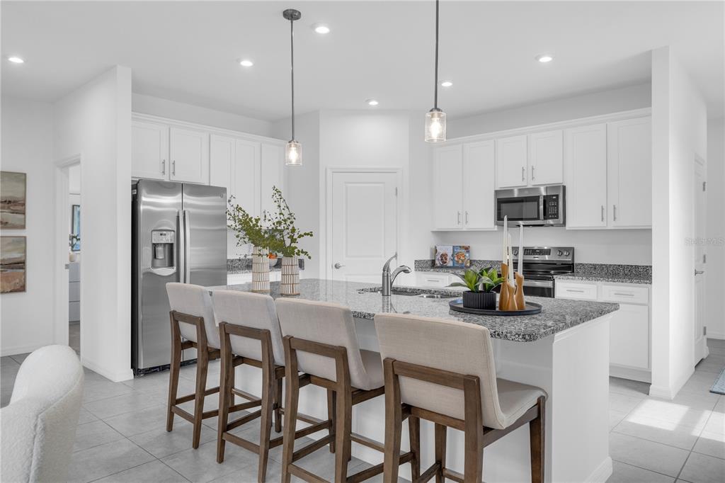 A modern kitchen features white cabinetry, granite countertops, a large island, and four bar stools — 10165 MORNING MEADOWLARK TRAIL, PARRISH, FL
