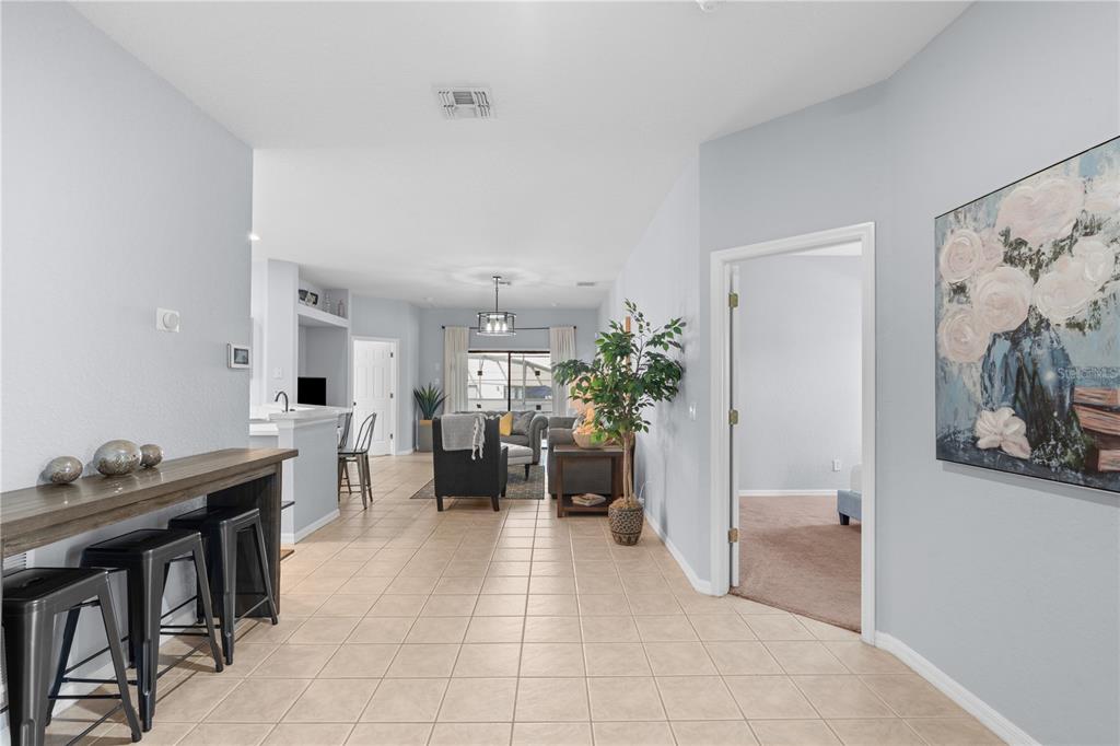 A tiled hallway leads to an open-concept living area with a breakfast bar and furniture — 16813 LAZY BREEZE LOOP, CLERMONT, FL