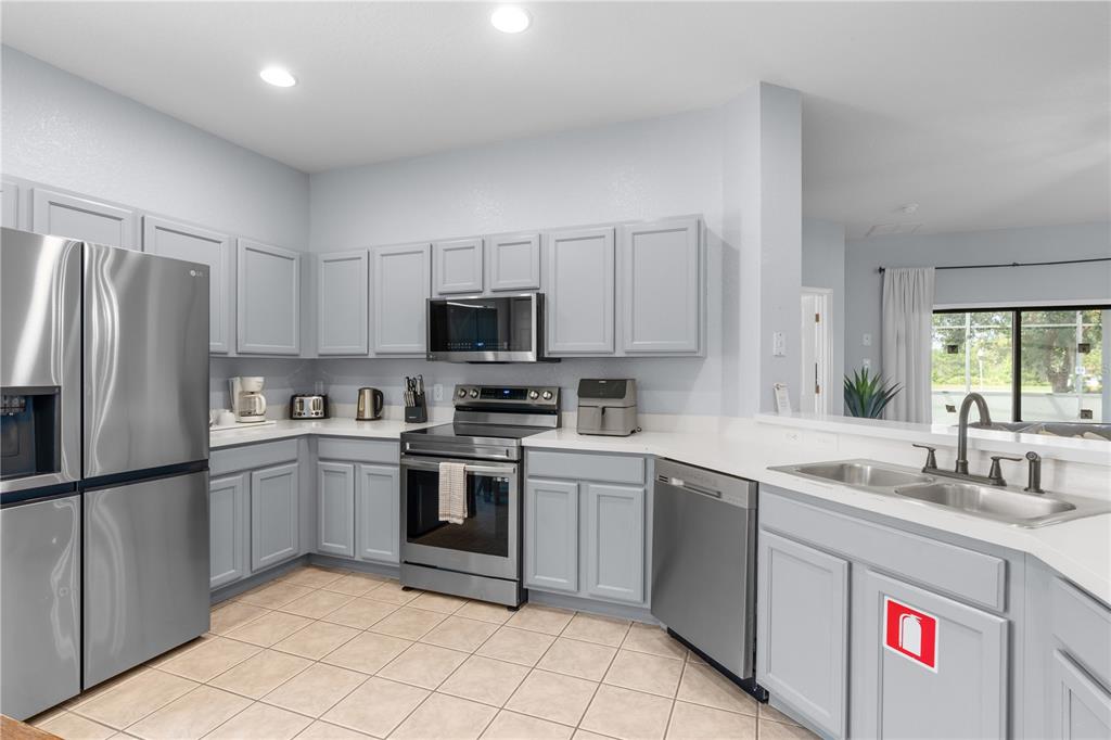 A kitchen features light gray cabinets, stainless steel appliances, white countertops, and tile flooring — 16813 LAZY BREEZE LOOP, CLERMONT, FL