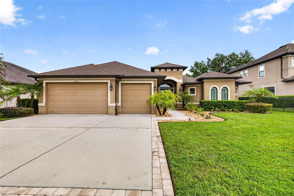 A single-story house with a two-car garage, tan stucco exterior, and a landscaped front lawn — 4760 LAGO VISTA CIRCLE, LAND O LAKES, FL