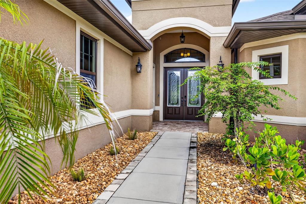 A paved walkway leads to the double front doors of a tan stucco house — 4760 LAGO VISTA CIRCLE, LAND O LAKES, FL