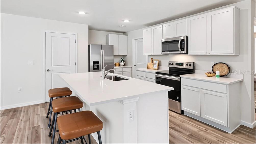 A modern kitchen features white cabinetry, a quartz-topped island with bar stools, and stainless appliances — 2106 NE 33RD LANE, OCALA, FL
