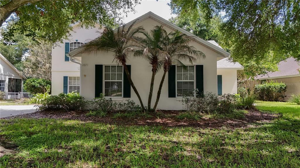 A white two-story house features dark shutters, two palm trees, and a landscaped front yard — 4875 ABACO DRIVE, TAVARES, FL